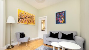 Un salon avec un canapé gris, un petit fauteuil, une table blanche et deux tableaux accrochés au mur.