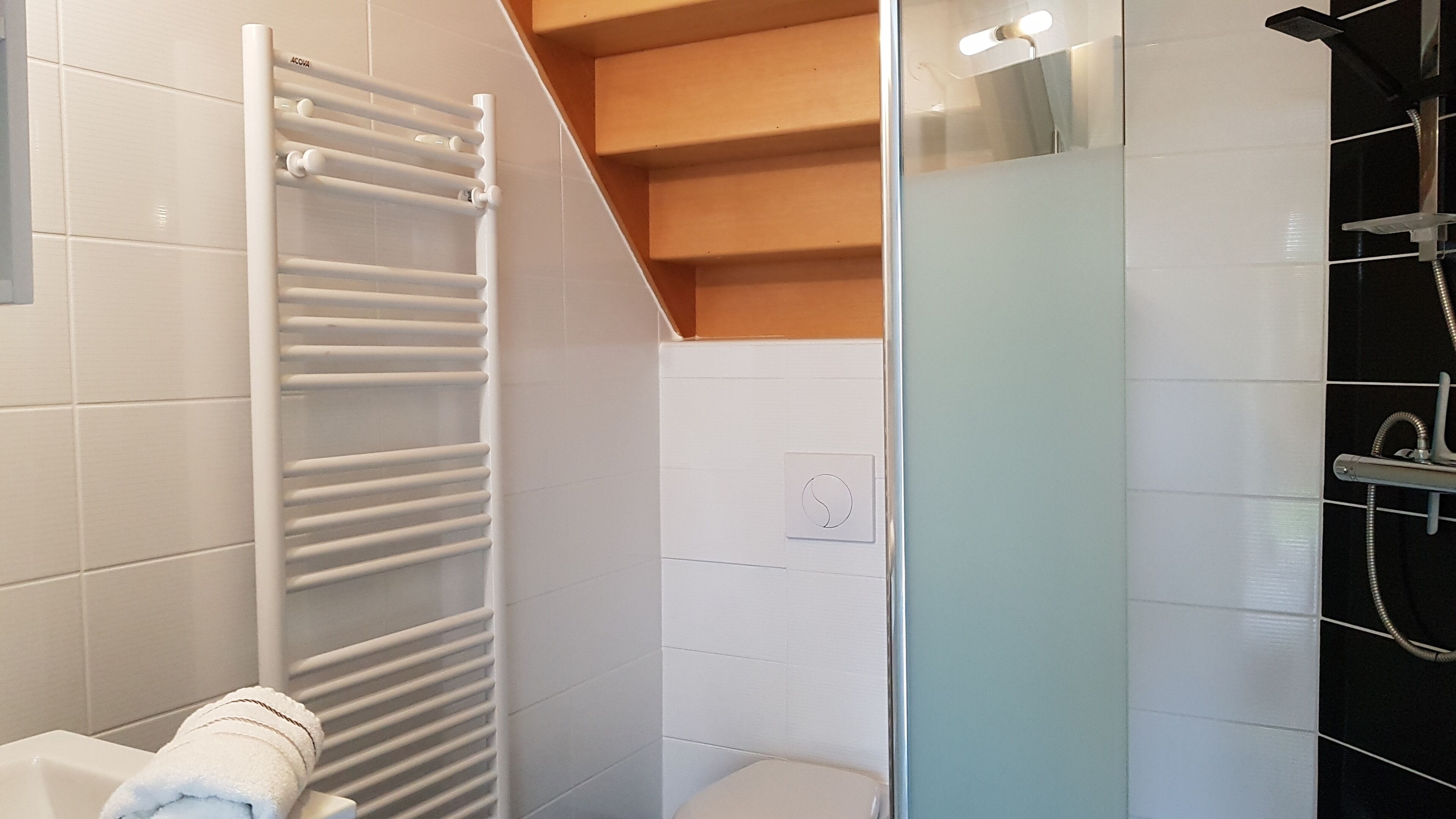 Een moderne badkamer met een douchecabine van glas, een witte handdoek op de vloer en een witte handdoekhouder.