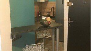 A compact kitchen with a black countertop, a small sink, and a bowl of fruit. There is a door to the right and a painting on the wall. - Charming 2-room apartment in town center, 5 minutes from the sea (Nice)