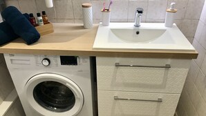 A compact bathroom with a washing machine, a sink, and a storage cabinet. - Charming 2-room apartment in town center, 5 minutes from the sea (Nice)