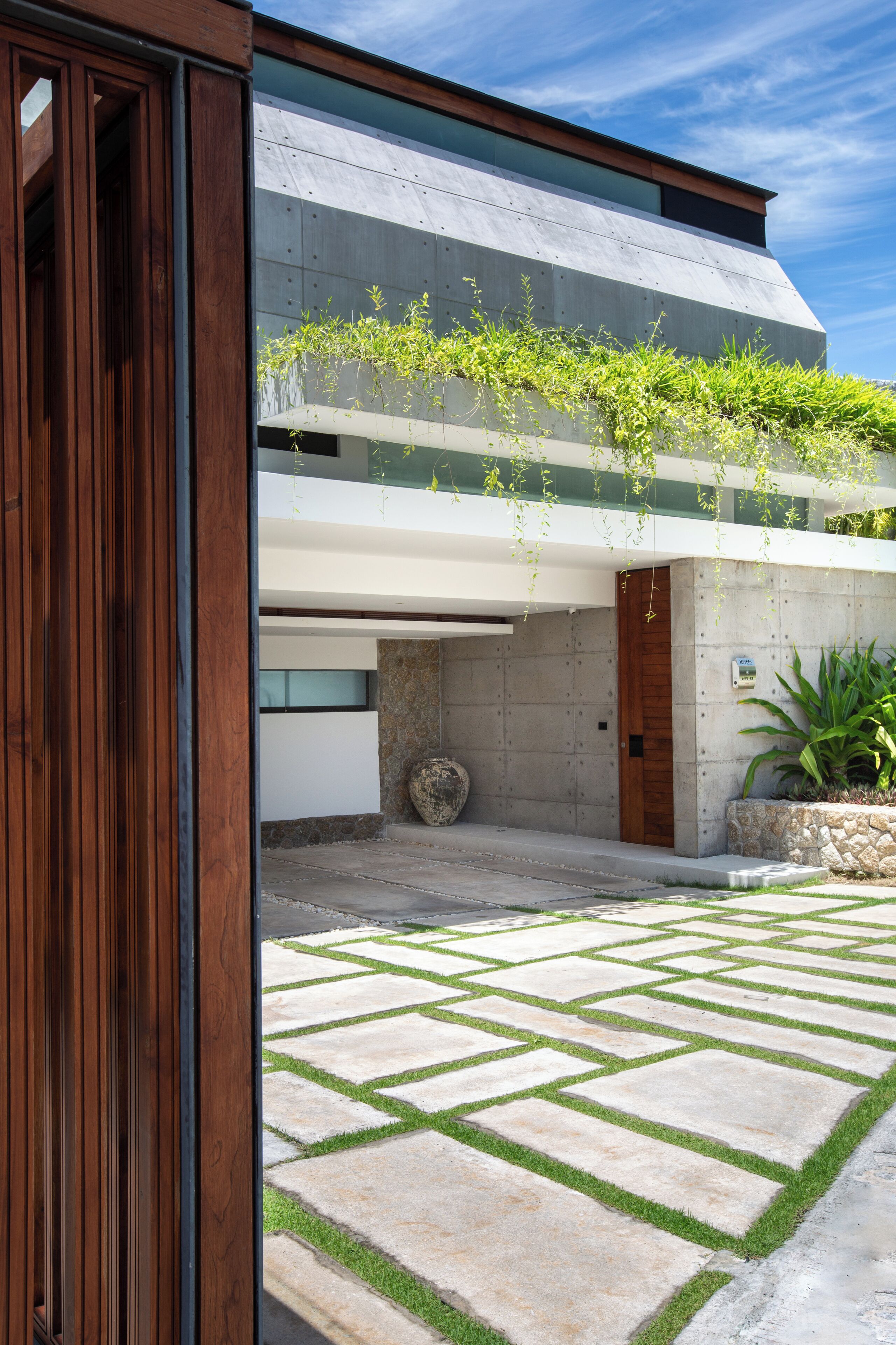 A modern building with a wooden door, a stone pathway, and a concrete wall with greenery.