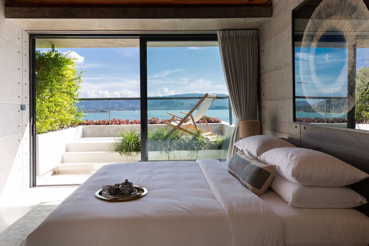 A bedroom with a large bed, a view of the sea, and a balcony with a chair.