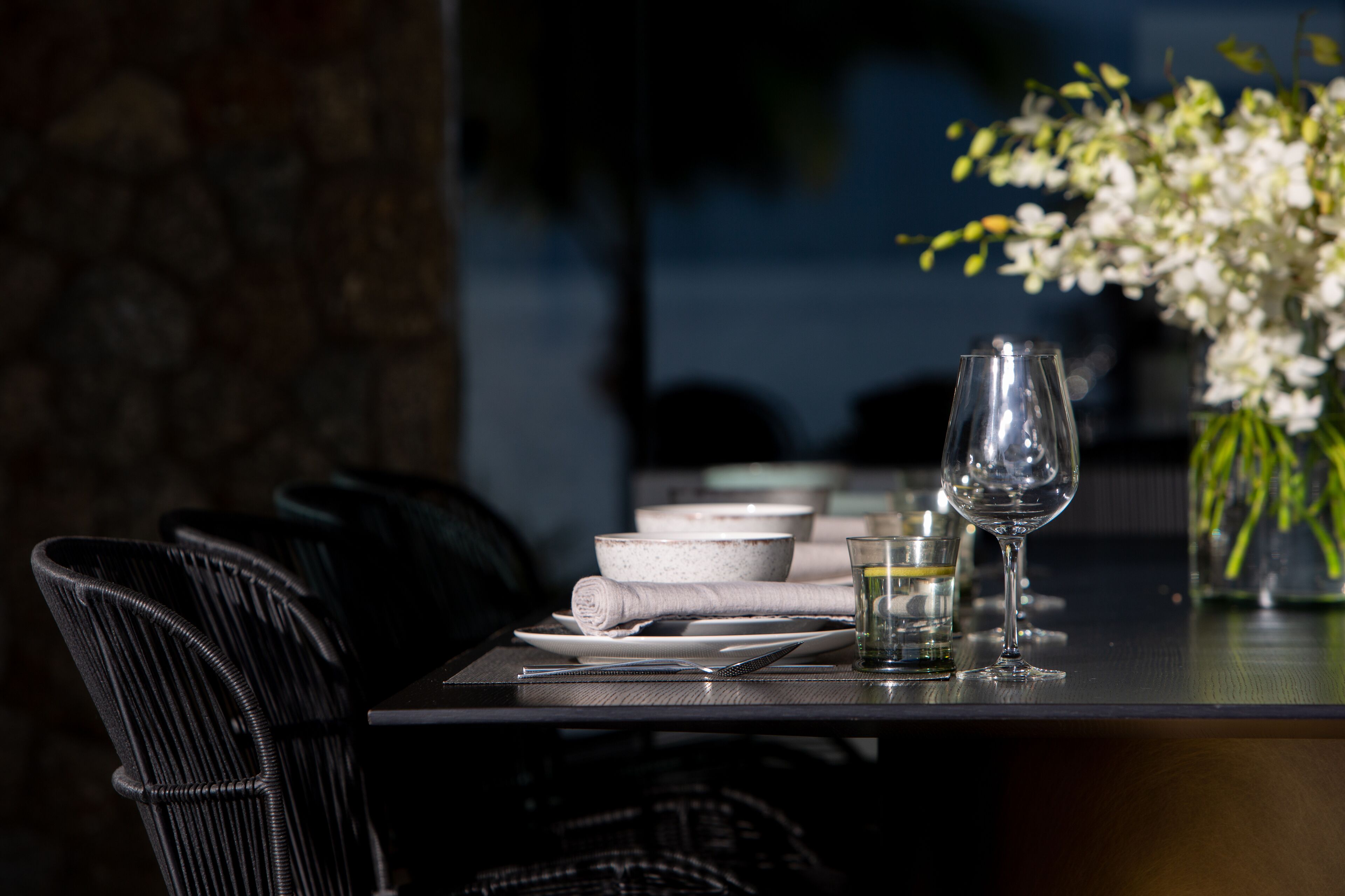 A dining table set with plates, bowls, a glass, and a wine glass, accompanied by black chairs.