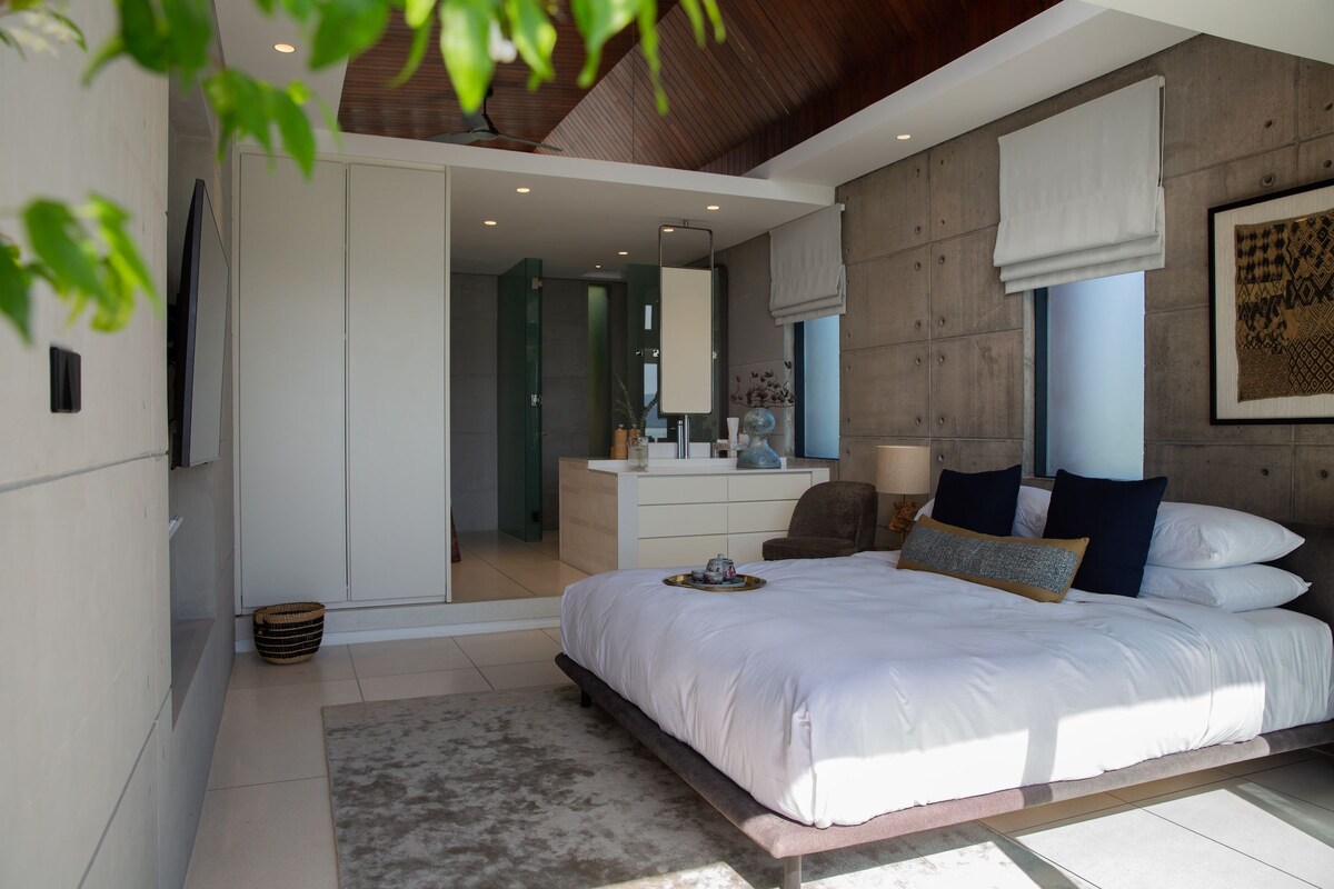 Une chambre moderne avec un grand lit, un bureau et une chaise. Il y a une fenêtre donnant sur l’extérieur.