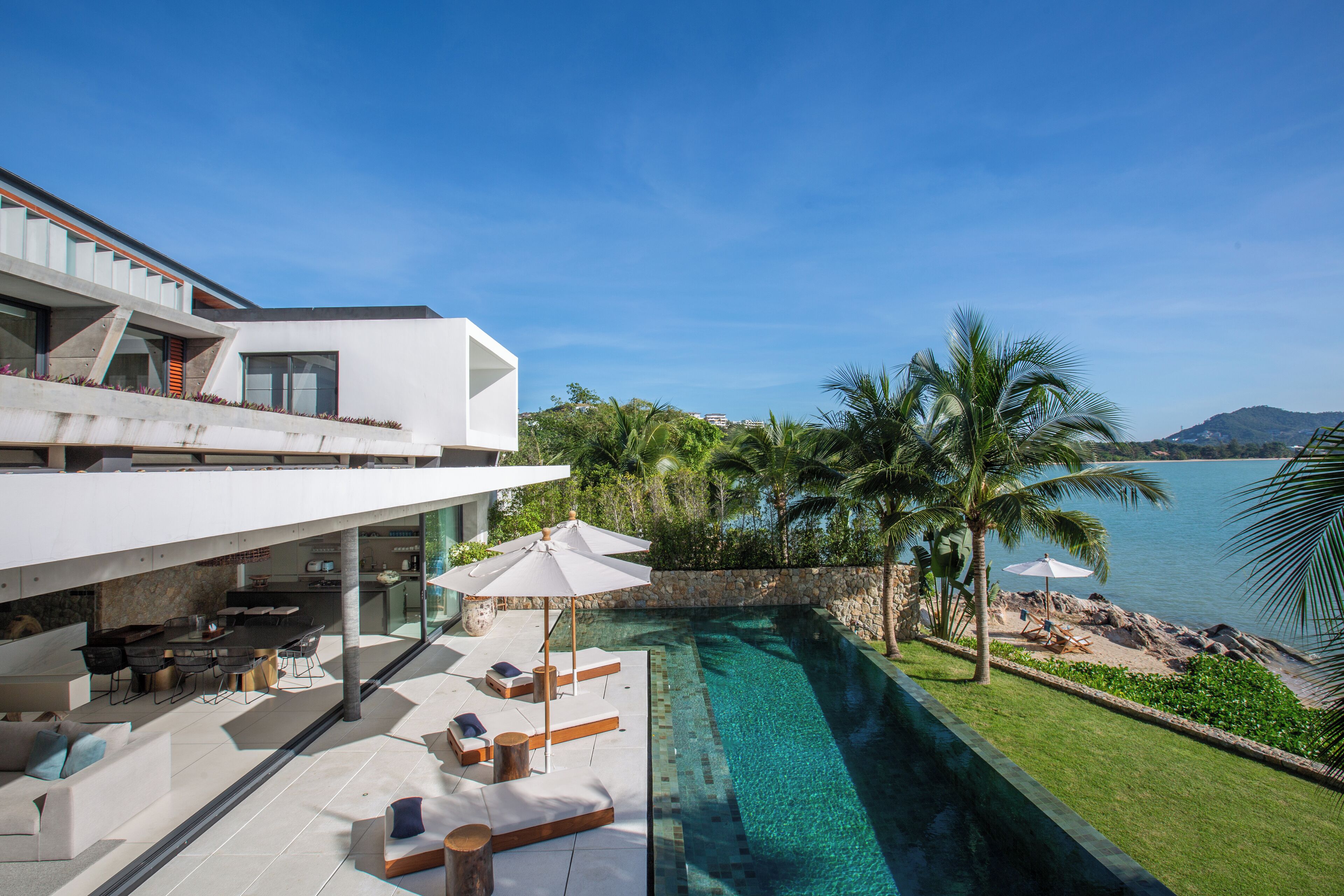 Una casa moderna con piscina, mobiliario de exterior y vista al mar.