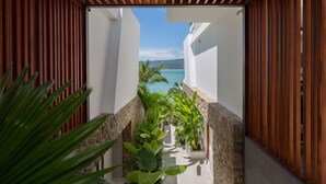 A narrow outdoor corridor with wooden slats and stone walls, leading to a balcony overlooking a beach and ocean. - Kerem Luxury Beachfront Villas (Koh Samui)