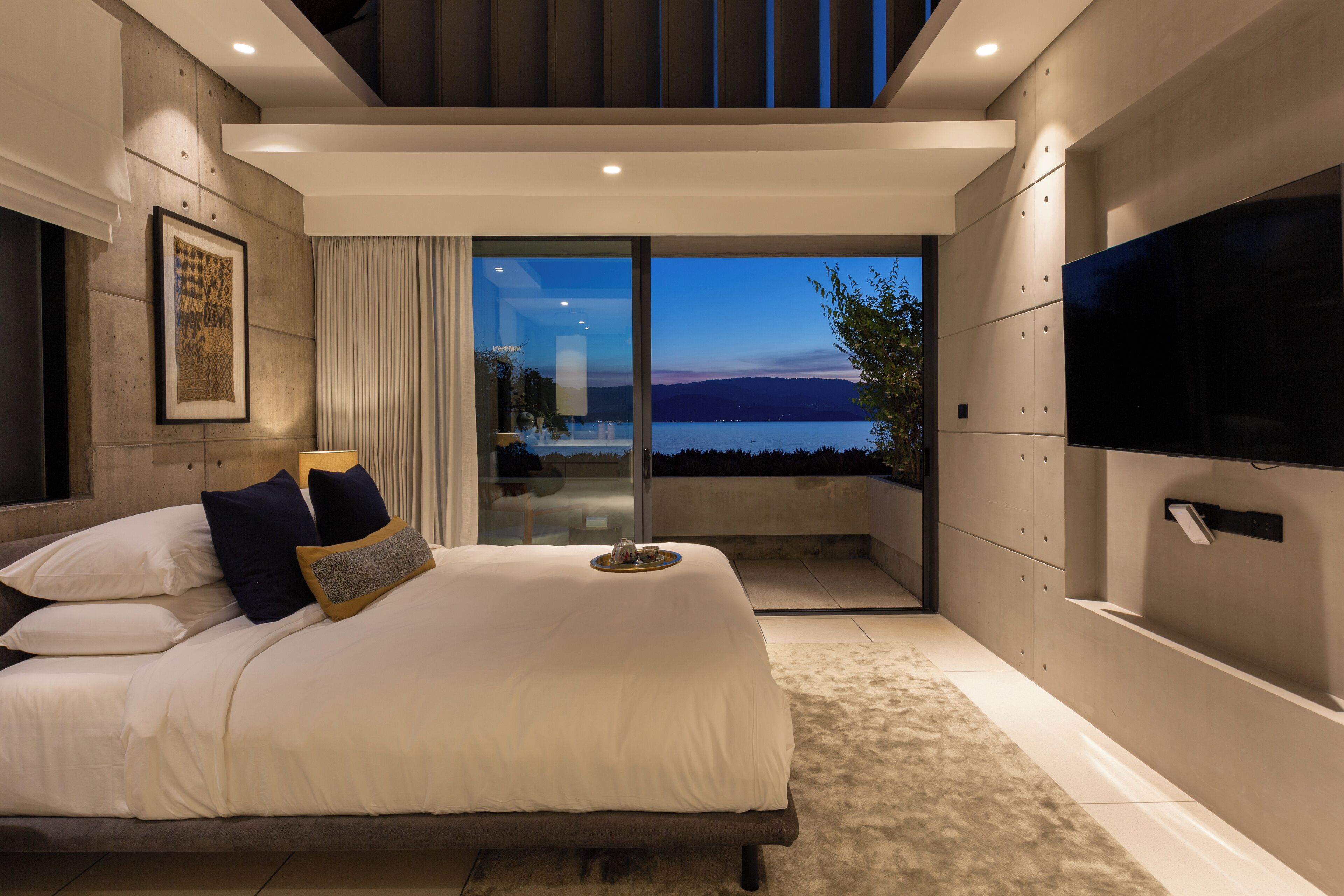 Un dormitorio moderno con una cama grande, un televisor de pantalla plana y un balcón con vistas al agua.