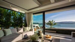A modern living room with a sofa, coffee table, and a view of the ocean. - Kerem Luxury Beachfront Villas (Koh Samui)