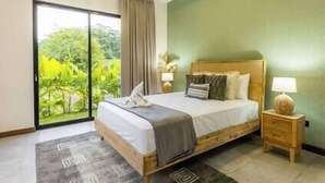 Une chambre à coucher avec un lit, une table de chevet, une lampe et une vue sur la verdure grâce à une porte coulissante.