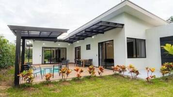 Een modern huis met twee verdiepingen, een overdekt terras, een zwembad en een keurig onderhouden gazon.