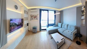 Una sala de estar moderna con un televisor de pantalla plana grande, un sofá seccional gris, una mesa de centro y un ventanal con vistas al exterior.