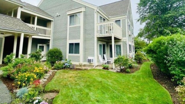 A two-story residential building with a balcony on the second floor, a covered porch, and a well-maintained lawn. - Stylish 2nd floor Ocean Edge condo (Brewster)