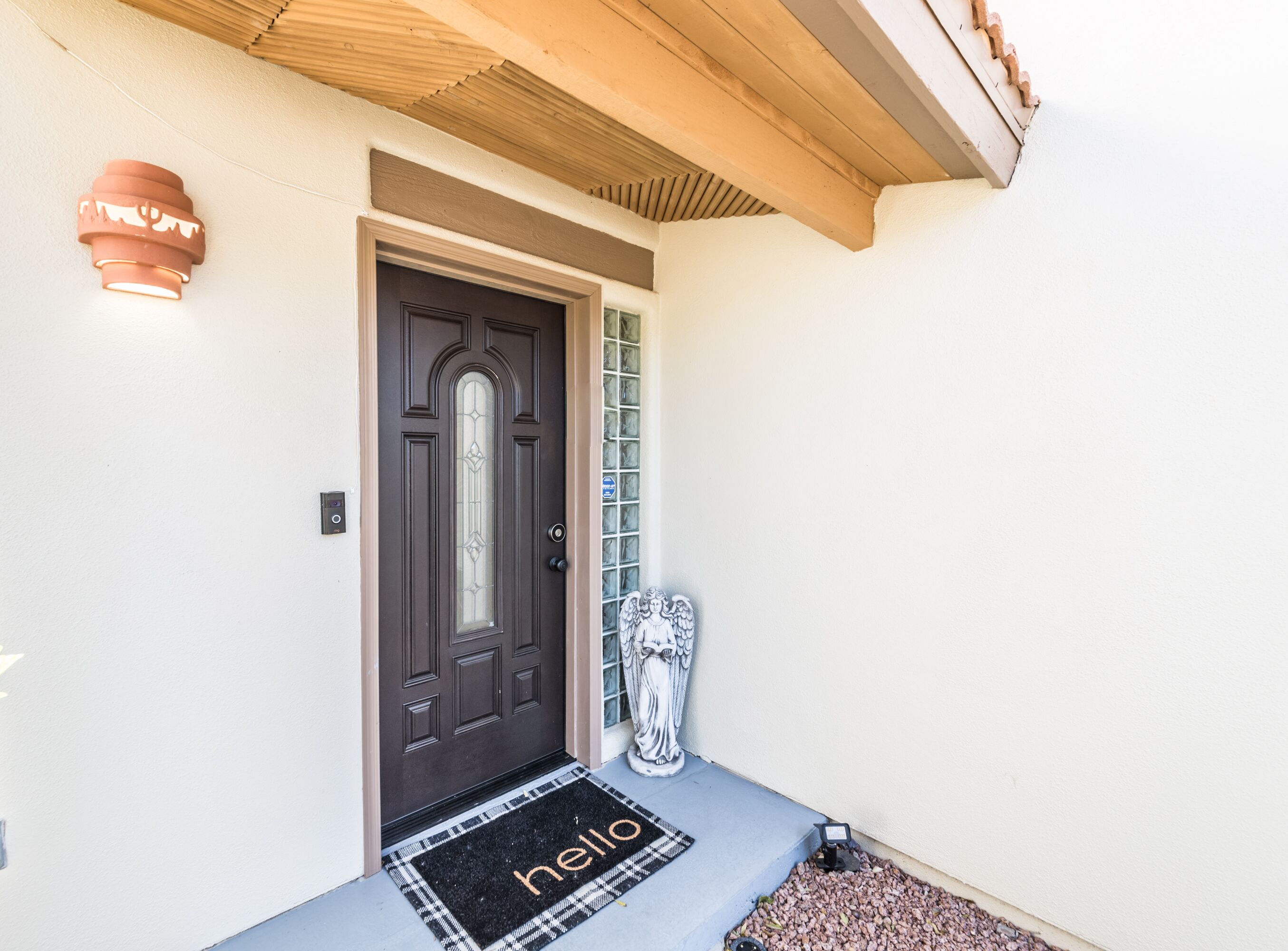 A dark brown door with a glass panel, a welcome mat with "hello" text, and a small statue of an angel.