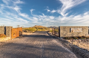 Un camino pavimentado que conduce a una puerta con un muro de piedra y un cartel que dice 'Alicante'.