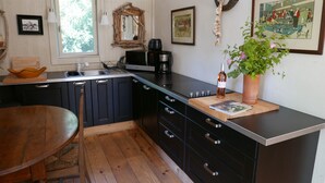 A modern kitchen with a wooden table, black cabinets, a coffee machine, and a potted plant. -  A quiet natural setting, a comfortable 60M2 apartment with swimming pool & bbq. (Saint etienne du gres)