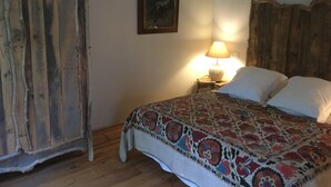 A bedroom with a wooden headboard, a patterned bedspread, a bedside lamp, and a framed picture on the wall. -  A quiet natural setting, a comfortable 60M2 apartment with swimming pool & bbq. (Saint etienne du gres)