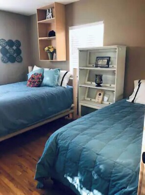A bedroom with two beds, wooden flooring, and a white wardrobe with shelves.