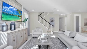 A modern living room with a large flat-screen TV, a sofa, a coffee table, and a staircase.