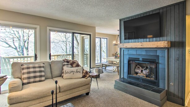 A cozy living room with a fireplace, a sofa with decorative pillows, and large windows offering a view of the outdoors. - Wintergreen Resort Condo: Walk to Ski Lift! (Wintergreen Resort)
