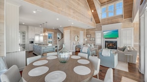 A spacious living area with a round wooden table, white sofas, and a fireplace. - 5BR Designer Home with Gulf Views, Elevator + Beach Access | Pelican Pointe (Destin)