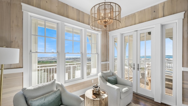 A spacious room with large windows, a wicker chandelier, and a view of the beach. - 5BR Designer Home with Gulf Views, Elevator + Beach Access | Pelican Pointe (Destin)