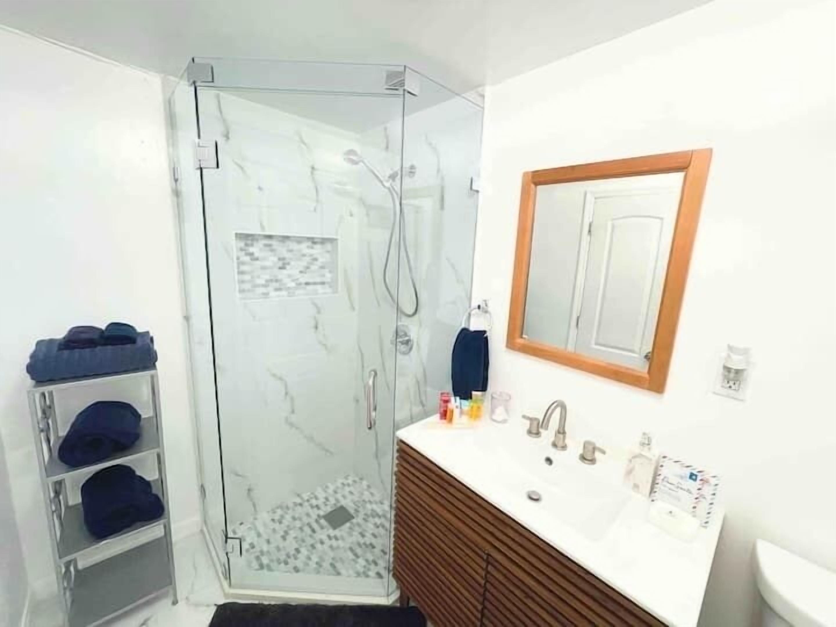 A bathroom with a glass shower enclosure, a wooden vanity with a sink, and a mirror above the vanity.