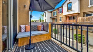 A balcony with a cushioned seating area, a large umbrella, and a view of neighboring houses.
