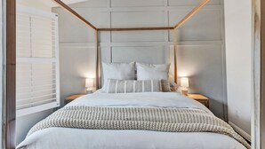 A bedroom with a four-poster bed, two bedside tables, and a window with blinds.