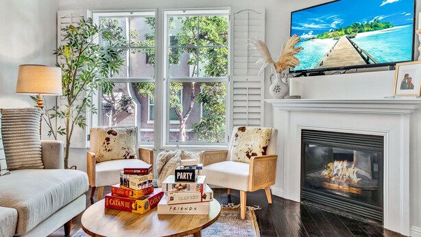 A living room with a fireplace, a television, and a view of a tropical beach through large windows.