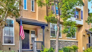 A two-story residential building with a front porch, a flag, and a well-maintained lawn.