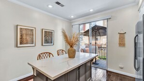 A modern kitchen with a marble countertop, wooden chairs, and a large window overlooking a balcony.