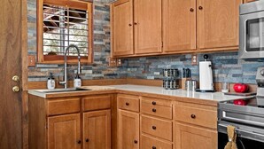 Una cocina con armarios de madera, salpicadero de piedra, pileta de acero inoxidable y microondas.