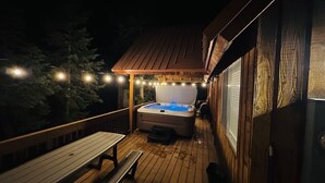 Una terraza de madera con un jacuzzi, un banco y luces colgantes.