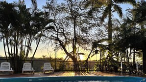 A pool area with chairs and a fence, surrounded by trees and a clear sky.