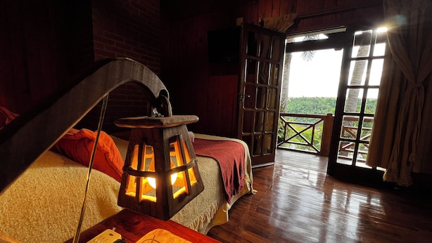 A wooden room with a bed, a lantern, and a wooden table with a remote control.