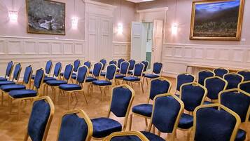 A conference room with rows of blue chairs and gold frames, white paneled walls, and framed artwork on the walls.