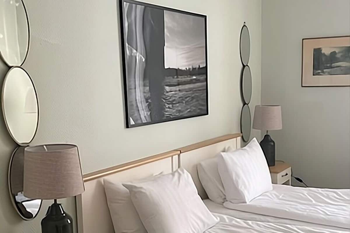Quarto com cama, duas mesas de cabeceira, abajur, espelho e um quadro na parede.