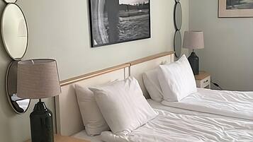 A bedroom with a bed, two bedside tables, a lamp, a mirror, and a framed picture on the wall.