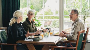 Una mesa de comedor con sillas, un jarrón con flores y una ventana con vistas al follaje.
