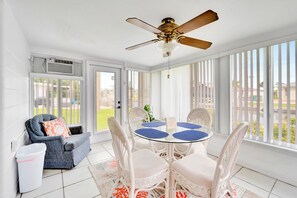 Relax in this serene sunroom with a sofa, chairs, and ceiling fan, surrounded by large windows.