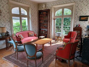 A cozy room with a red sofa, blue chairs, a wooden table, and a large bookshelf.