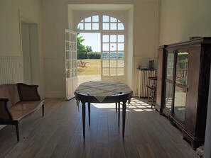 A room with a large arched doorway leading to an outdoor area, a round table with a tablecloth, a dark wooden cabinet, and a wicker sofa.