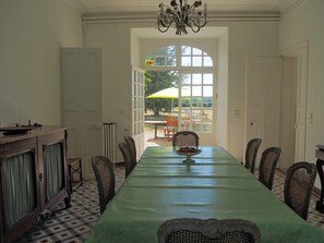 A dining room with a long table, chairs, a chandelier, and a view through a large window.