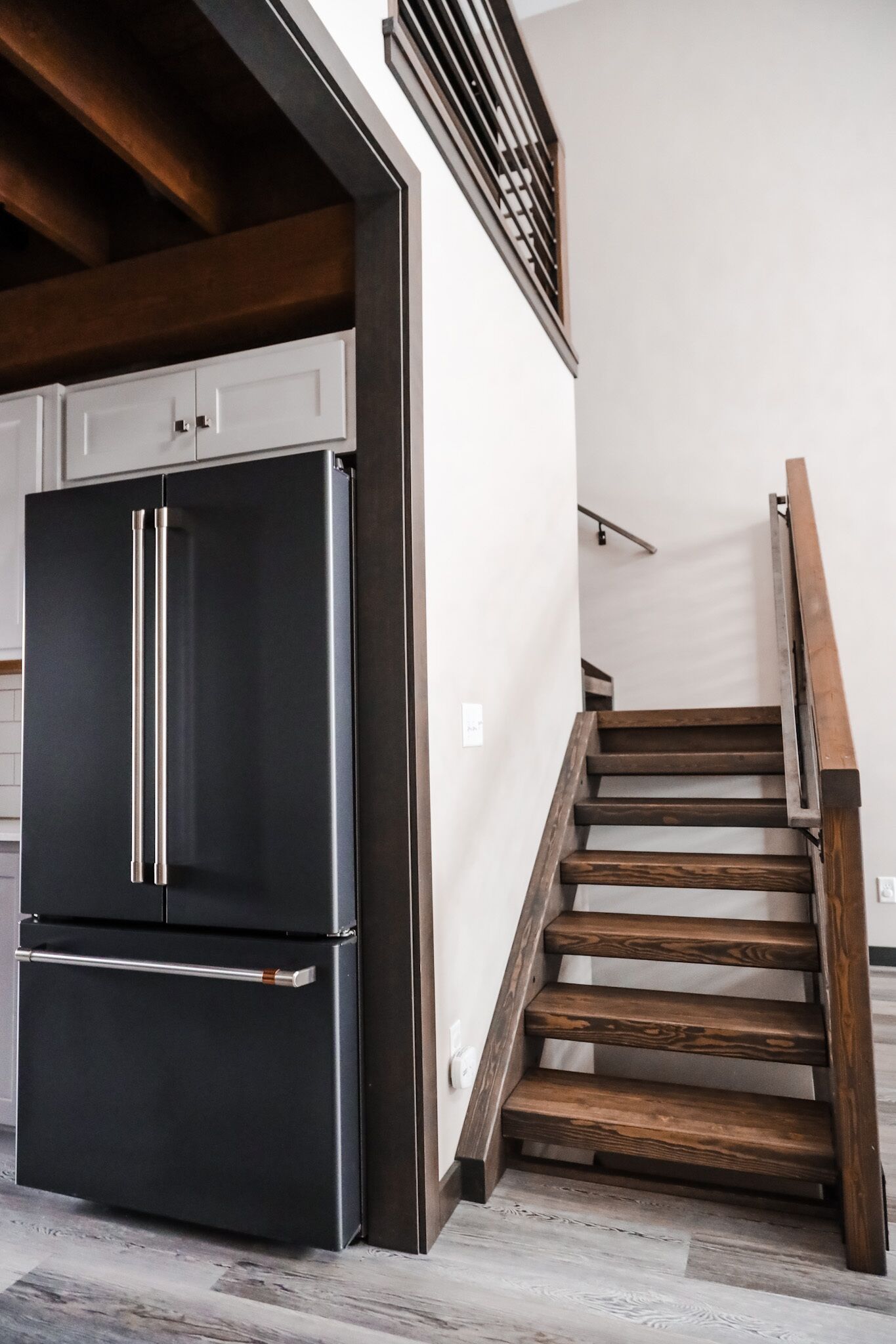 Une cuisine moderne avec un réfrigérateur en acier inoxydable, un escalier en bois et un mur blanc.