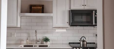 A modern kitchen with white cabinets, a stainless steel sink, a microwave, and an oven.