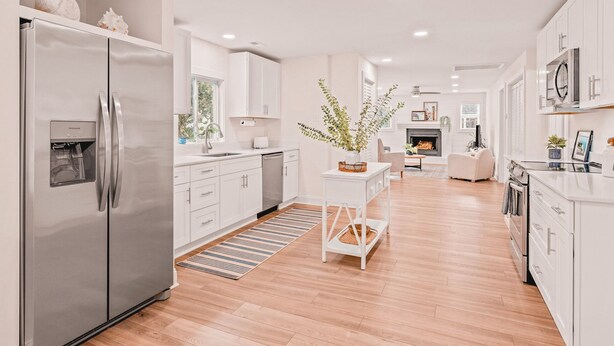 Cocina moderna con refrigerador de acero inoxidable, armarios blancos, una isla central y una chimenea en la sala de estar.