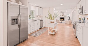 Cocina moderna con refrigerador de acero inoxidable, armarios blancos, una isla central y una chimenea en la sala de estar.