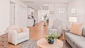 Una sala moderna con un sofá, un sillón y una mesa de centro, una cocina al fondo y un pasillo que conduce a un comedor.