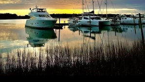 Marina con varios yates amarrados, agua tranquila y un cielo al atardecer.