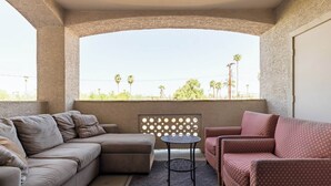 A balcony with a beige sofa, a patterned armchair, and a small round table.